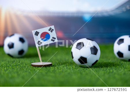 South Korean flag miniature stand with soccer balls on green artificial grass, symbolizing international sports competition and national team pride in a stadium atmosphere South Korean flag miniature stand with soccer balls on green artificial grass, symbolizing international sports competition and national team pride in a stadium atmosphere 127672591