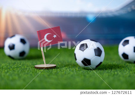 Miniature Turkish flag proudly displayed with soccer balls on green grass, against a stadium backdrop, symbolizing national team pride and international football competition 127672611