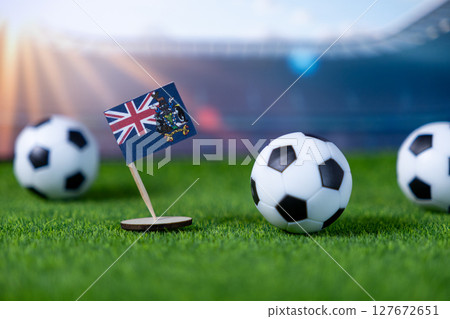 Flag of South Georgia and South Sandwich Islands stands prominently on green grass with soccer balls, symbolizing national pride for upcoming international sports 127672651