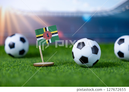 Dominica's national flag with soccer balls on a green football pitch, symbolizing international sports competition and national pride in stadium Dominica's national flag with soccer balls on a green football pitch, symbolizing international sports competition and national pride in stadium 127672655