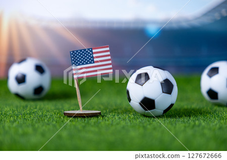 Miniature American flag on lush green grass with soccer balls, representing national pride and sportsmanship for US football, ready for stadium championship 127672666
