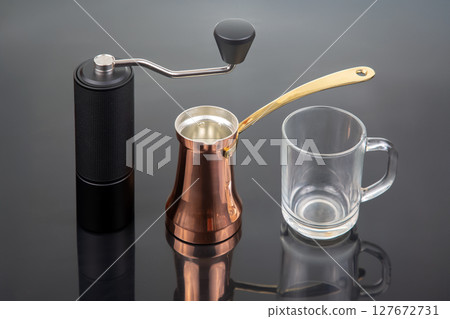 A black manual coffee grinder with a metallic handle, a copper cezve  127672731