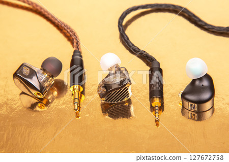 Three earbuds with woven cables and gold-plated jacks on a reflective golden surface Three earbuds with woven cables and gold-plated jacks on a reflective golden surface 127672758