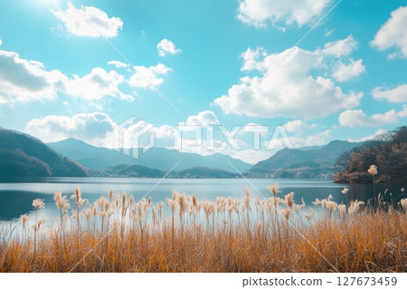 A beautiful lake with a cloudy sky in the background. The lake is surrounded by tall grass and mountains in the distance A beautiful lake with a cloudy sky in the background. The lake is surrounded by tall grass and mountains in the distance 127673459