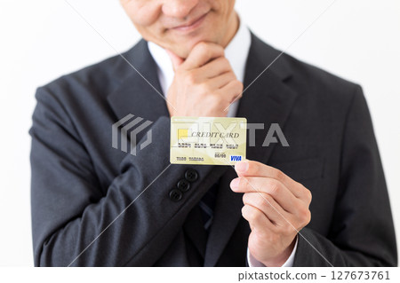 A businessman in a suit holding a credit card and worrying A businessman in a suit holding a credit card and worrying 127673761