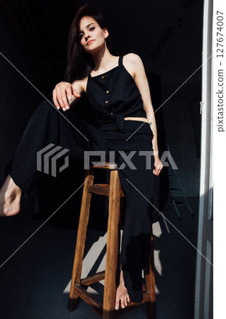 fashionable woman in black clothes sitting on chair in room fashionable woman in black clothes sitting on chair in room 127674007