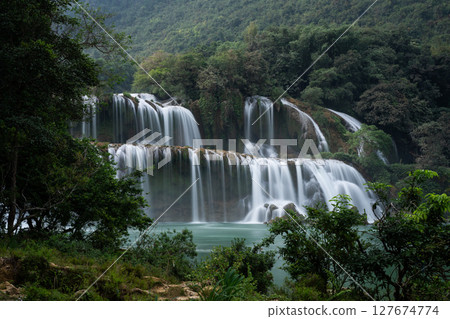 Detian Falls cascading water flowing through lush green vegetation in Vietnam 127674774