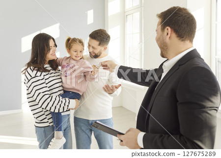 Realtor giving house keys to a happy young family standing in empty new apartment. Realtor giving house keys to a happy young family standing in empty new apartment. 127675289