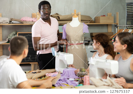 Experienced black sewing teacher guiding adult beginners in practical workshop Experienced black sewing teacher guiding adult beginners in practical workshop 127675337