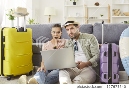 Surprised couple sitting on floor, looking at laptop screen, planning trip shocked by prices. Surprised couple sitting on floor, looking at laptop screen, planning trip shocked by prices. 127675340