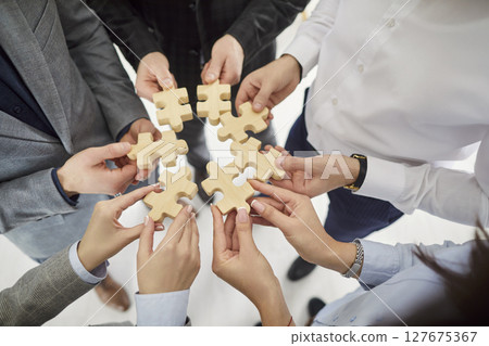 Business team connecting wooden puzzle pieces in circle, showing unity, collaboration and teamwork. 127675367