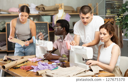Young male teacher helping students sew while other drawing paper 127675370