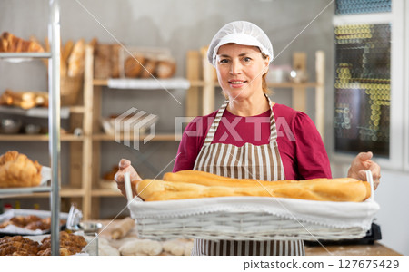 Adult female baker with basket of baguettes Adult female baker with basket of baguettes 127675429