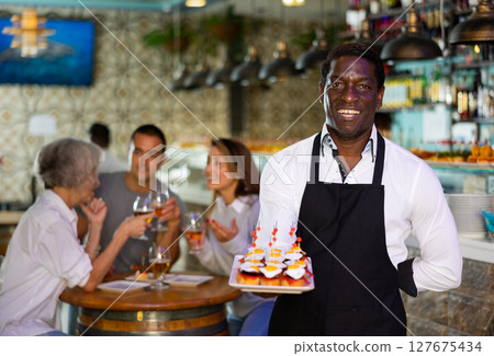 Professional african american waiter holding serving tray for restaurant guests 127675434