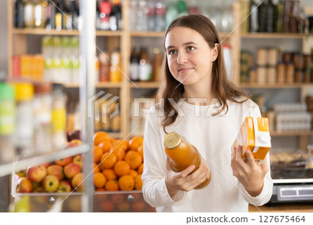 Teen girl hold packages bottles and choose consider juice in store 127675464