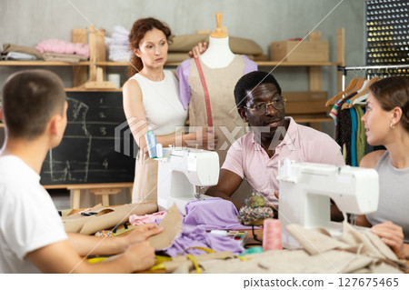 Middle-aged man talking with woman and sewing, other working with mannequin Middle-aged man talking with woman and sewing, other working with mannequin 127675465