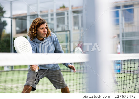 Focused adult man playing paddle tennis outdoors Focused adult man playing paddle tennis outdoors 127675472