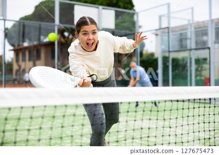 Sporty young girl playing padel on open court Sporty young girl playing padel on open court 127675473
