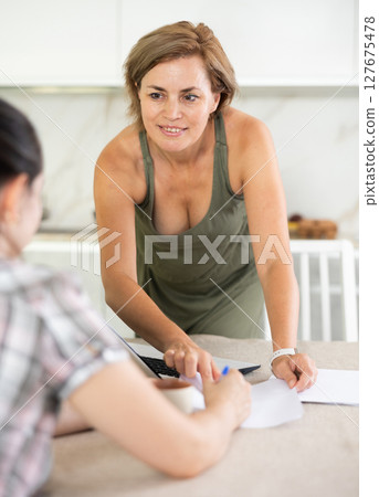 Two middle-aged women having business conversation in the kitchen Two middle-aged women having business conversation in the kitchen 127675478