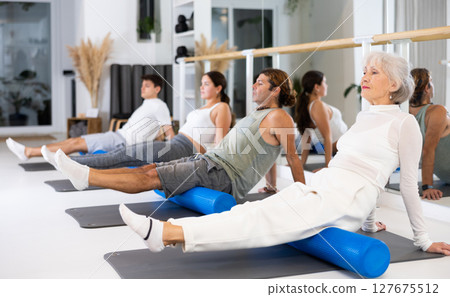 Sports people practicing pilates with rolled mats at group class in yoga studio Sports people practicing pilates with rolled mats at group class in yoga studio 127675512