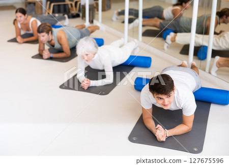 Women and men practicing yoga positions during group training in fitness center, performing stretching asana Urdhva Mukha Shvanasana 127675596