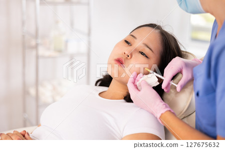 Professional cosmetologist hands in rubber gloves performing lips enhancement treatment to female client, making injection of lip fillers Professional cosmetologist hands in rubber gloves performing lips enhancement treatment to female client, making injection of lip fillers 127675632