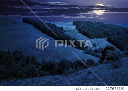 tranquil countryside landscape with forest on the hill in summer at night. green environment with tree on mountain under blue sky for travel. rolling highland in full moon light tranquil countryside landscape with forest on the hill in summer at night. green environment with tree on mountain under blue sky for travel. rolling highland in full moon light 127675691