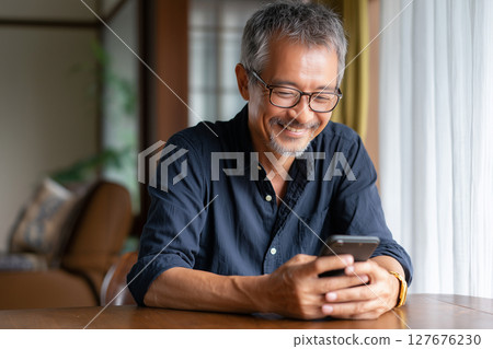 Senior man enjoying using his smartphone at home (AI generated image) 127676230