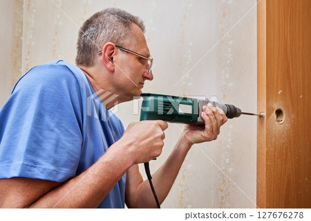 Drilling hole for latch installer drives spade bit into wooden door edge while holding drill steady to create proper opening for latch insertion and alignment. 127676278