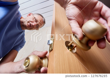 Inserting locking mechanism into predrilled hole of wooden door to prepare for secure attachment of door knob and ensure proper function of locking system by installer. Inserting locking mechanism into predrilled hole of wooden door to prepare for secure attachment of door knob and ensure proper function of locking system by installer. 127676285