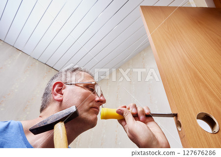 Removing wood from door edge with chisel to create precise recess for latch plate ensuring secure fit of locking mechanism by skilled carpenter. Removing wood from door edge with chisel to create precise recess for latch plate ensuring secure fit of locking mechanism by skilled carpenter. 127676286