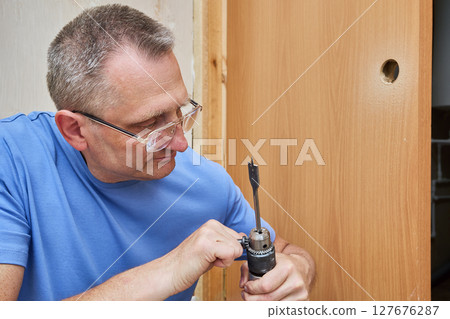 Carpenter uses chuck key to secure spade bit inside drill chuck. 127676287