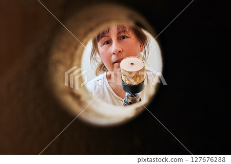 Completing hole cutting woman shows power drill with wood core inside hole saw viewed through circular opening made for latch on wooden door surface. Completing hole cutting woman shows power drill with wood core inside hole saw viewed through circular opening made for latch on wooden door surface. 127676288