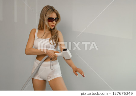 Woman tunes a laser hair removal machine. She holds a working part of the epilator in her hands and poses for a photo. Body Care. Underarm Laser Hair Removal. 127676349