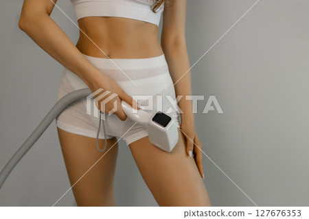 Woman tunes a laser hair removal machine. She holds a working part of the epilator in her hands and poses for a photo. Body Care. Underarm Laser Hair Removal. 127676353