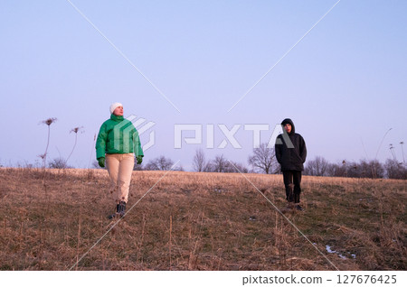 Twilight stroll across an open field with friends enjoying nature's tranquility and warm attire in early evening light, embracing the serene moment together 127676425