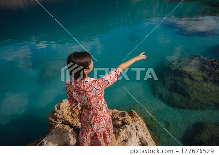 Woman stands on Mediterranean Sea coast, embracing cool, off-season atmosphere with waves crashing on shore and overcast sky above. serene, peaceful moment on quiet beach. 127676529