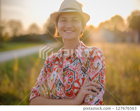 Young woman walking through picturesque European field in late summer. Golden sunlight, lush greenery, and serene rural atmosphere create peaceful countryside scene. Young woman walking through picturesque European field in late summer. Golden sunlight, lush greenery, and serene rural atmosphere create peaceful countryside scene. 127676563