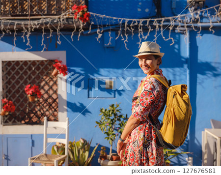 Woman in dress strolls through colorful streets of coastal town of La Vila Joiosa or Villajoyosa. Colorful homes in seaside villa of Villajoyosa in Southern Spain 127676581