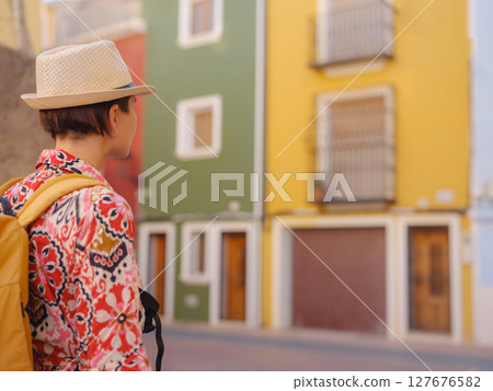 Woman in dress strolls through colorful streets of Spanish coastal town of La Vila Joiosa or Villajoyosa. sunny winter atmosphere highlights charm of Mediterranean architecture and quiet seaside life 127676582