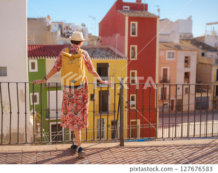 Woman in dress strolls through colorful streets of Spanish coastal town of La Vila Joiosa . sunny winter atmosphere highlights charm of Mediterranean architecture and quiet seaside life, back view 127676583
