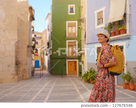Woman in dress strolls through colorful streets of Spanish coastal town of La Vila Joiosa or Villajoyosa. sunny winter atmosphere highlights charm of Mediterranean architecture and quiet seaside life 127676586