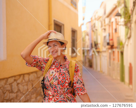 Woman in dress strolls through colorful streets of Spanish coastal town of La Vila Joiosa or Villajoyosa. sunny winter atmosphere highlights charm of Mediterranean architecture and quiet seaside life 127676591
