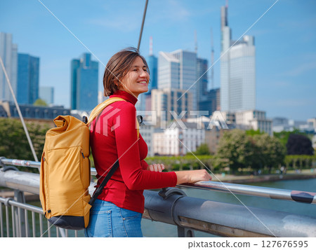 Tourist woman explores modern Frankfurt, walking through vibrant streets with contemporary architecture, skyscrapers, and urban spaces, enjoying lively atmosphere of modern side. 127676595
