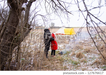 Exploration and warmth in a winter landscape with a bright tent and two figures embracing amidst nature's chill at an outdoor campsite Exploration and warmth in a winter landscape with a bright tent and two figures embracing amidst nature's chill at an outdoor campsite 127676617