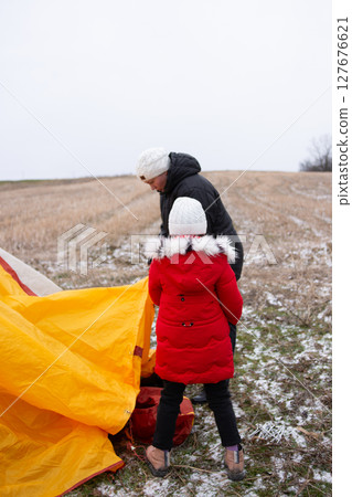 Preparing for a winter adventure as a child and adult set up a bright yellow tent in a snowy field under overcast skies Preparing for a winter adventure as a child and adult set up a bright yellow tent in a snowy field under overcast skies 127676621
