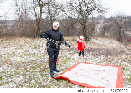 Setting up a winter camping tent on a snowy hillside with family enjoying quality time outdoors in a serene landscape 127676622