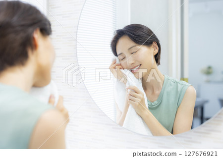 A woman washing her face and wiping it with a towel A woman washing her face and wiping it with a towel 127676921