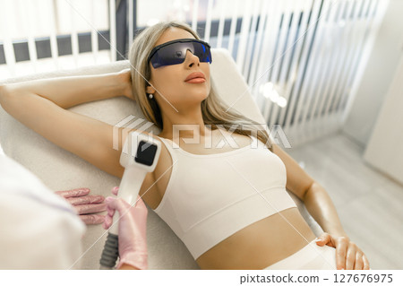 Hair removal procedure. Cropped shot of young fit woman client receiving laser hair removal procedure on body in beauty clinic. Women beauty and cosmetology concept 127676975