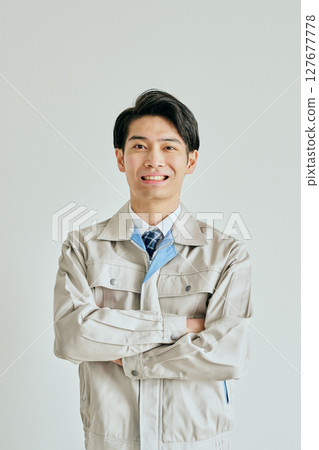 A young man in work clothes with his arms folded A young man in work clothes with his arms folded 127677778
